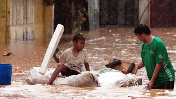 A father and son wade through flood water using a crude flotation device in the impoverished Tumana riverside community in Manila in August 2012 © Jason Gutierrez/IRIN